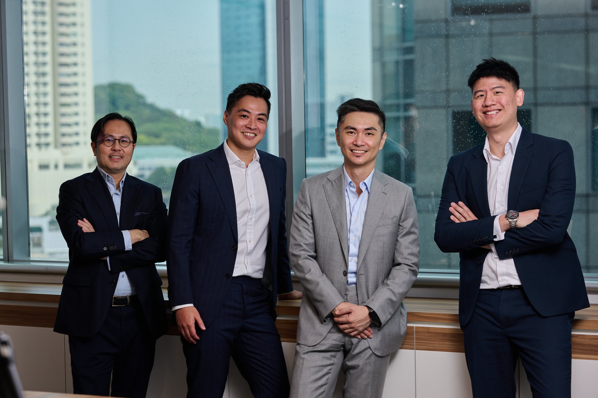 Aura Private Equity Singapore team standing together in with their arms crossed and leaning against a window