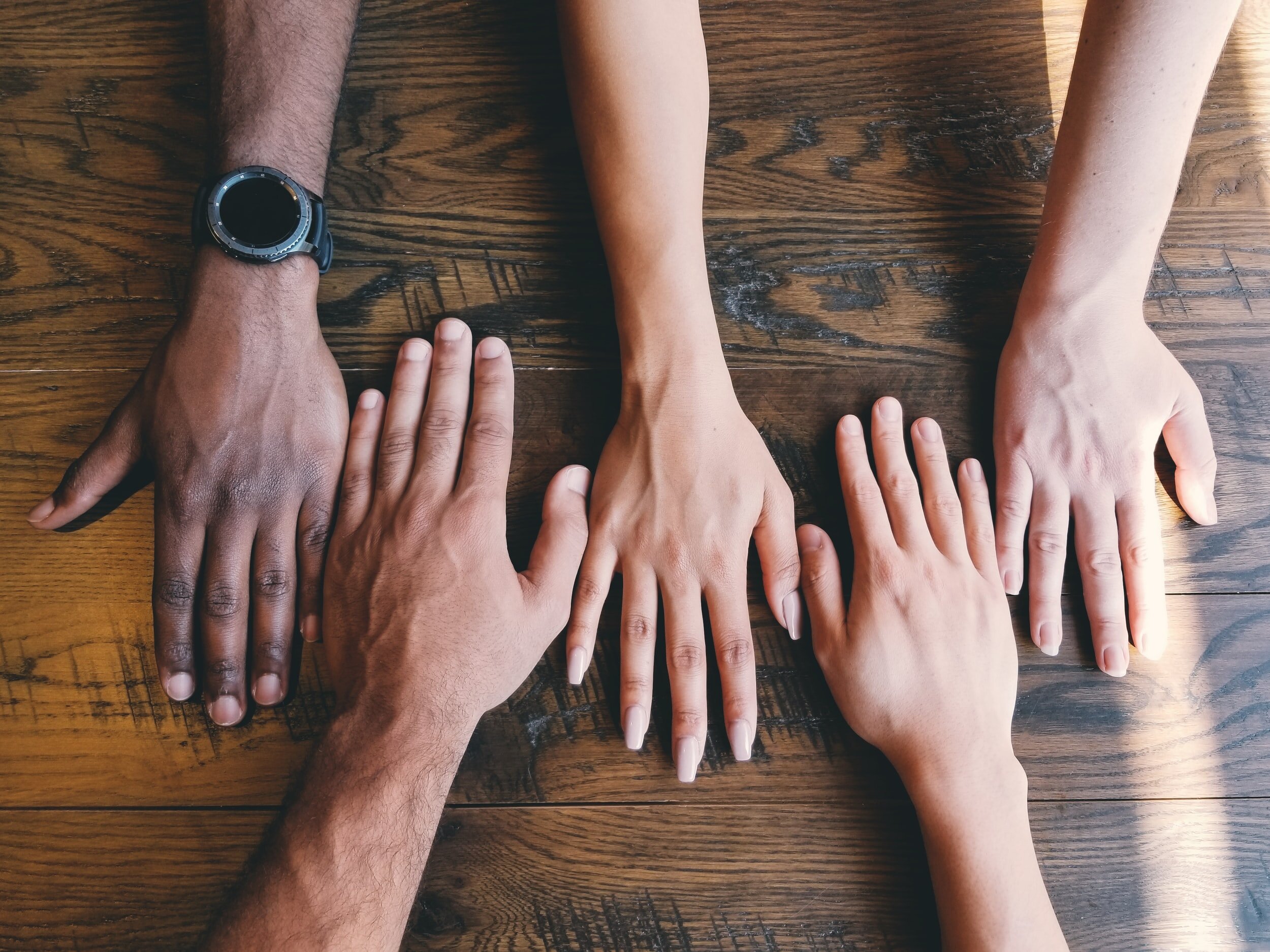 Four hands of varying skin tones lined up on a wooden table