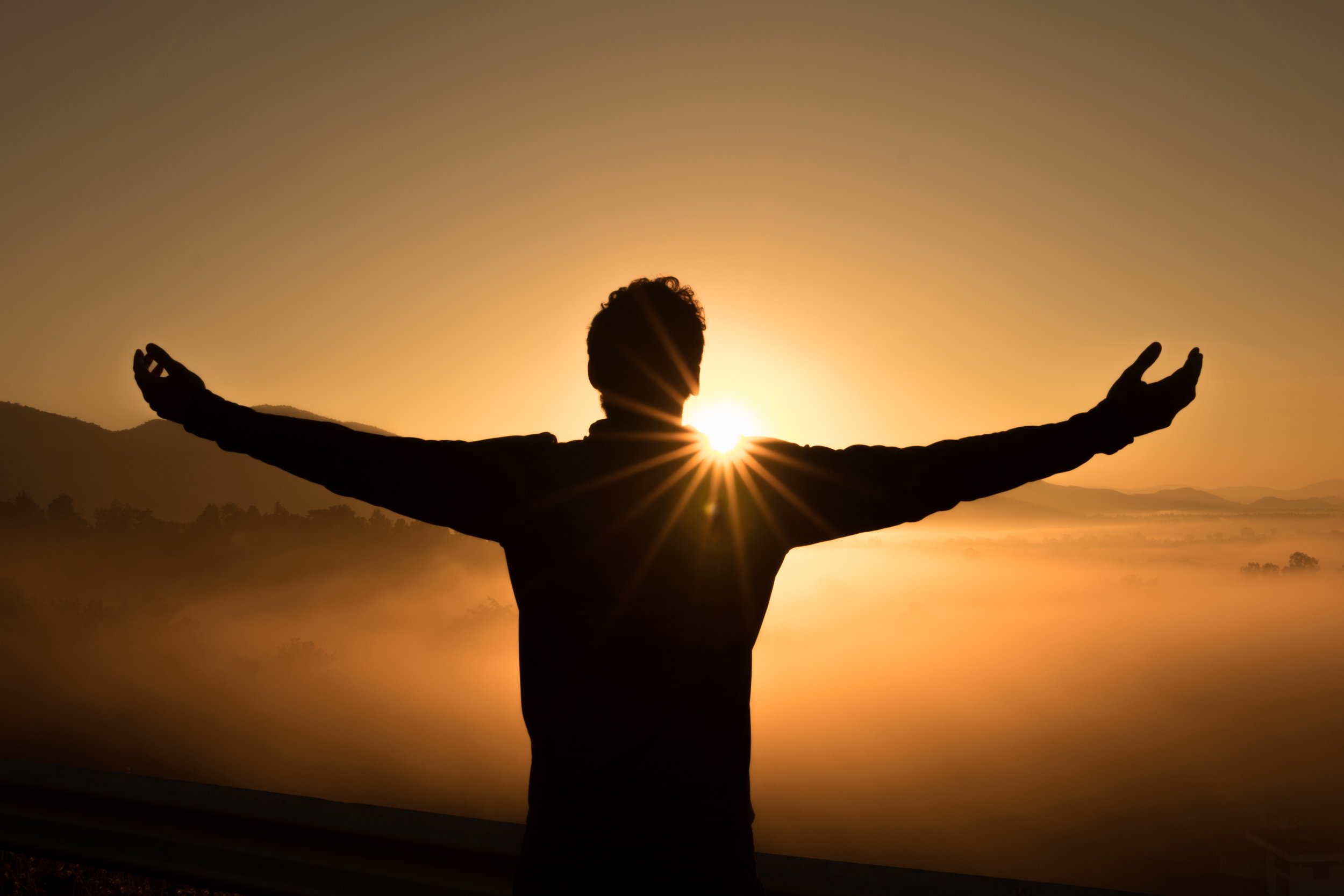 Back lit person holding their arms out toward the sun